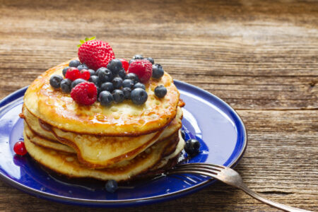 Pile of pancakes with  fresh berries on blue plate